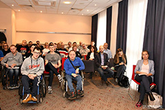 W sali konferencyjnej grupa uczestników, z przodu osoby na wózkach